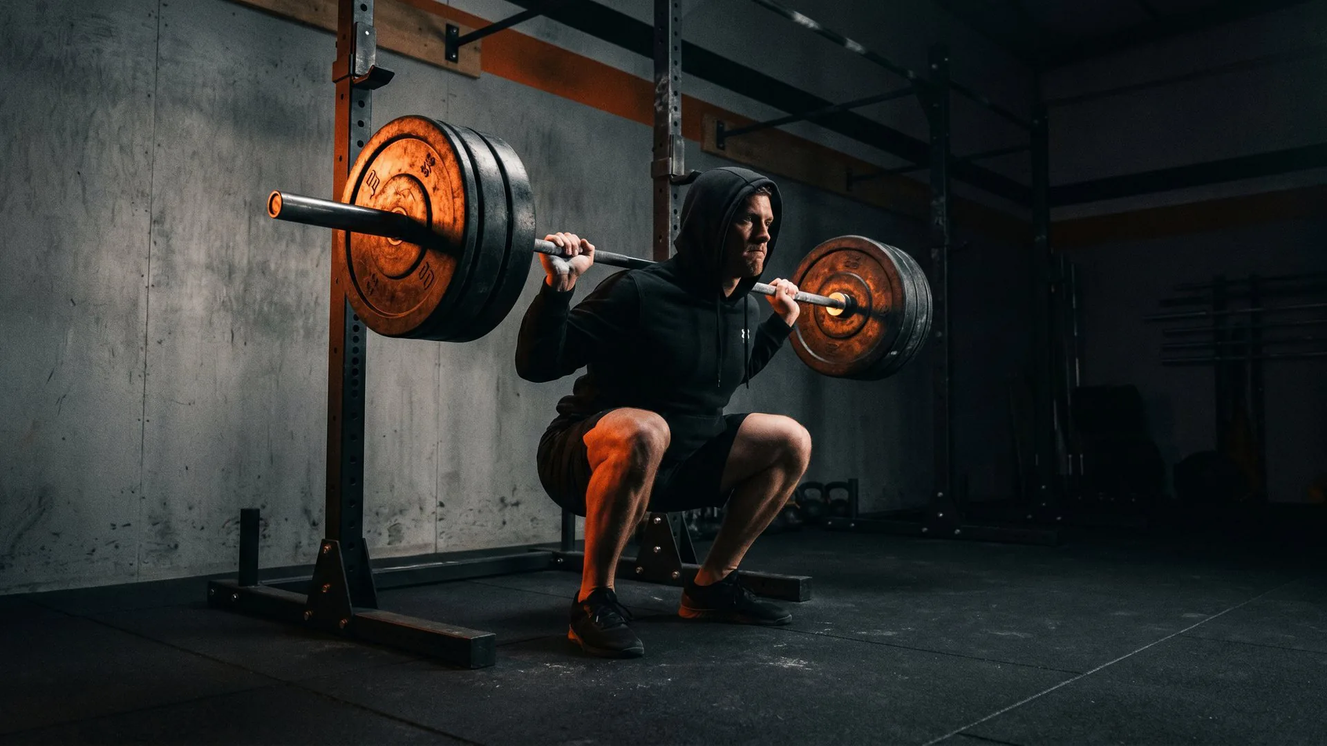 Barbell loaded with plates racked in a squat cage in a dimly lit gym, Flame Orange rim light catching the knurling — a strong squat setup ready for a working set